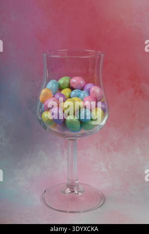 Tiny pastel colored Easter eggs in wine glass against beutiful colorful background in pink and blue shades. Stock Photo