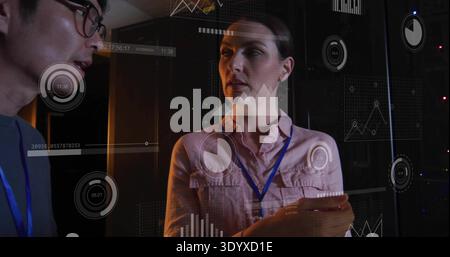 Reviewing woman holding tablet wearing blue lanyard in data center, with server racks and analytics Stock Photo