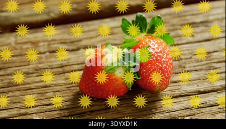 Showing two ripe red strawberries sitting on rustic wooden plank, with yellow star graphic overlays Stock Photo