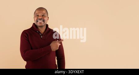 Smiling black man pointing aside with hand while posing on beige background Stock Photo