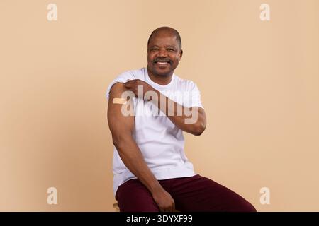 Mature black man in casual clothing showing bandage on his upper arm Stock Photo