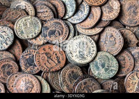 A high-angle, close-up shot of a dense pile of ancient Roman bronze coins. The coins exhibit various stages of oxidation and patina, with colors rangi Stock Photo