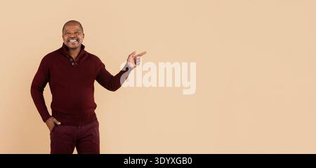 Black man in sweater pointing to aside with hand on beige background Stock Photo