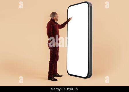 Mature black man touching blank screen of giant smartphone on beige background Stock Photo