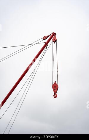 Red crane jib with hook and pulley system against overcast sky at Tollesbury Stock Photo