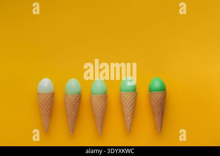 Green easter eggs in waffle cones on yellow background Stock Photo