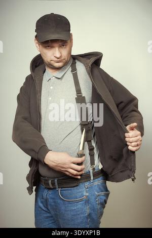 Man in black hooded shirt and black hat showing his dagger Stock Photo