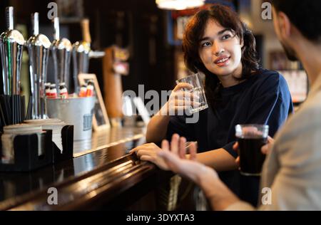 Young woman drinks beer and talks to man at bar Stock Photo