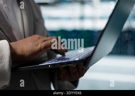 Close up of data center admin using laptop to update systems, protecting servers from easily exploitable software vulnerabilities. Employee using notebook, looking for errors slowing down servers Stock Photo