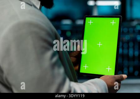 Close up of programmer in data center using isolated screen tablet to check for server performance issues. IT professional in server hub fixing errors slowing down hardware using chroma key device Stock Photo