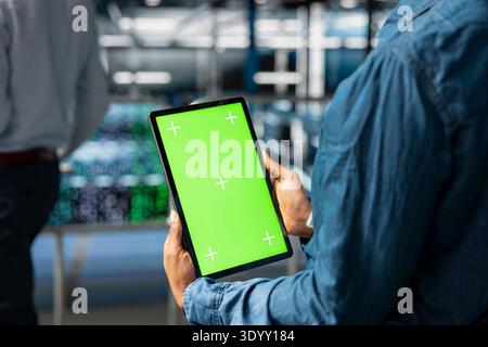 Server hub technician brainstorming using chroma key tablet to review diagnostics in data center. Employee on elevated industrial platform solving tasks looking at isolated screen. Stock Photo