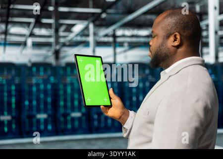 Close up of data center admin using green screen tablet in data center, auditing systems for vulnerabilities. African american server hub worker using mockup device, troubleshooting issues Stock Photo