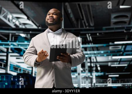 Engineer in server room overseeing mainframes gear used for managing databases. African american man in data center establishment doing checkup on rackmounts storing information Stock Photo