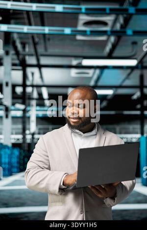 Computer scientist in data center using diagnostic tools and system monitoring software on laptop to identify root cause of errors. IT specialist in server farm facility repairing equipment Stock Photo