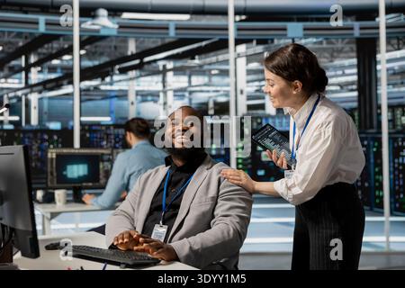 Engineers in data center sharing laugh at desk during job break from infrastructure maintenance tasks. Engineering team enjoying lighthearted moment while working in server room Stock Photo