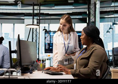 Friendly IT expert teaching intern to use artificial intelligence. Jolly manager guiding junior dev through AI tool integration, mentoring her on using machine learning APIs Stock Photo