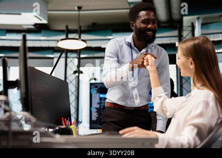 Tech company team leader doing fist bump with intern in office, satisfied with work done Happy office manager satisfied with progress of junior dev learning how to use machine learning tech Stock Photo