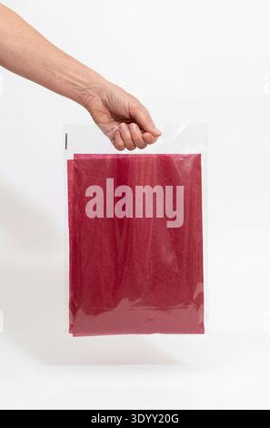 Mockup of a clear plastic bag with a handle, held by a hand, containing red tissue paper. Stock Photo