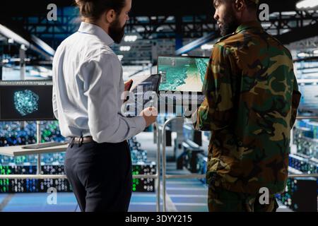 Black military soldier works with engineer to strengthen national defense systems, protecting national servers in a huge data center. Using artificial intelligence for armed forces operations. Stock Photo
