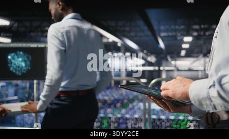 Close up of data center software developer doing maintenance tasks on tablet, ensuring optimal performance. Worker reviewing diagnostics and applying patches to server hub equipment, Stock Photo