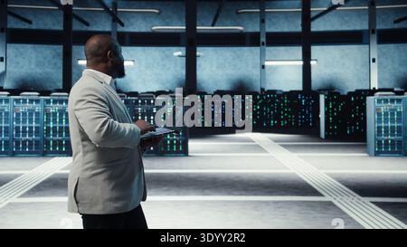 Server room system administrator using laptop to do infrastructure AI machine learning automatization. IT expert in high tech data center doing maintenance using artificial intelligence, camera A Stock Photo