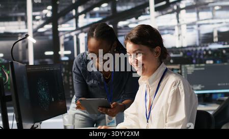 Smiling technicians doing fist bump in data center after successful deployment of AI tools. Server room engineering team celebrate completion of machine learning system integration, camera A Stock Photo