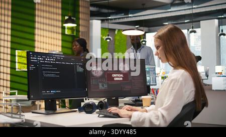 Female engineer in startup office struggling to fix critical error warning popup. Intern doing maintenance on computer glitches while coding in software development agency, camera A Stock Photo