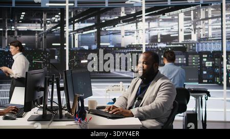 Lead data center technician overseeing team integrating AI automation in infrastructure rigs. Worker under server hub manager supervision using deep learning models for operational tasks, camera A Stock Photo