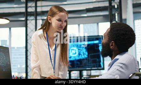 Young engineer and coworker with paraplegia doing brainstorming in office, reviewing AI system metrics. Junior dev and colleague in wheelchair talking, tuning neural networks using PC, camera A Stock Photo