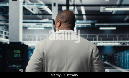 Admin walking in high tech data center facility, checking equipment for system stability. IT specialist overseeing server room, configuring supercomputers, optimizing performance, camera B Stock Photo