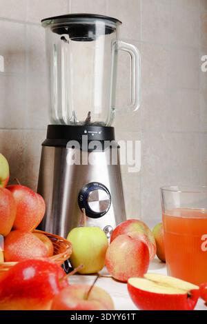 Modern stainless steel blender on a kitchen counter surrounded by fresh red and green apples, with a glass of fresh apple juice in the foreground. Hig Stock Photo
