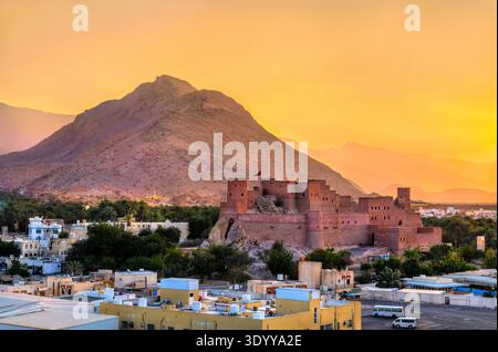 The majestic Nakhal Fort perched on a rocky outcrop against the backdrop of Hajar Mountains and a warm sunset sky in Oman. Stock Photo