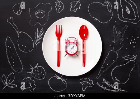 Top view on plastic forks and clock on white plate at black background Stock Photo