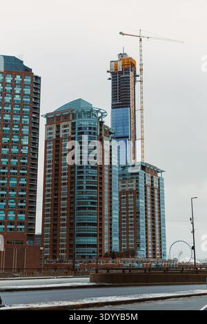 Workers continue the construction of a tall building close to the water as other buildings surround the site during a winter day. Stock Photo