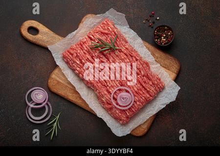 Raw minced beef with rosemary and onion rings on a wooden board Stock Photo
