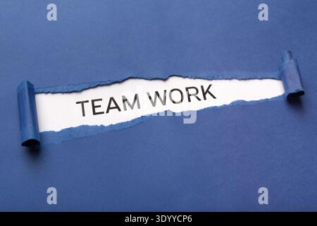Text Team work on white background appearing behind torn blue paper Stock Photo