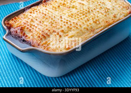 Homemade shepherd's pie in a blue brown ceramic dish on a blue ribbed placemat on a wood background backdrop. Stock Photo