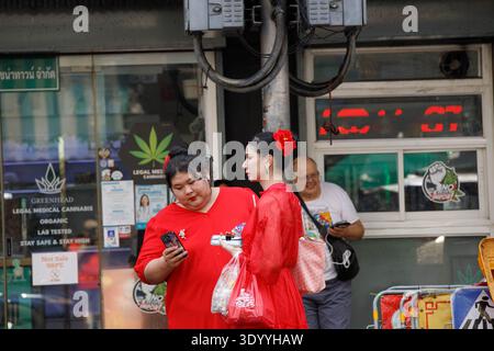 BANGKOK, THAILAND-FEB 15, 2026: Two women in red dresses shopping in market, Thai weekend market lifestyle, wide view, at Yaowarat. Stock Photo