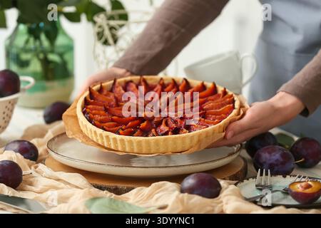 Woman holding tasty plum pie at table in kitchen Stock Photo