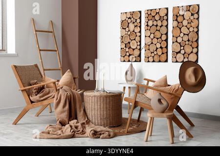 Interior of living room with armchairs, ladder and candle holders on wicker coffee table near white wall Stock Photo
