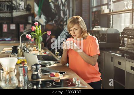 Happy middle-aged woman barista working on laptop Stock Photo