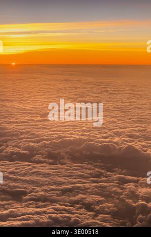 Sun sinks below the horizon while clouds stretch across the sky, creating an orange glow in the background. The view is captured from the window of an Stock Photo
