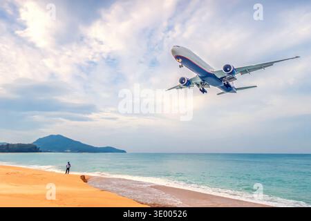 A view of the horizon of an airplane flying over a beach with ocean waves and distant clouds during daylight hours. Tours to tropical countries Stock Photo