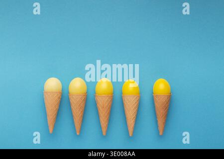 Yellow easter eggs in waffle cones on blue background Stock Photo