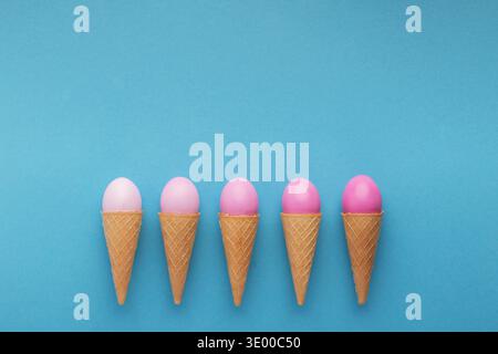 Pink easter eggs in waffle cones on blue background Stock Photo