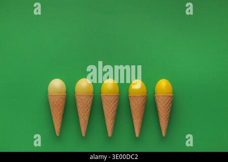 Yellow easter eggs in waffle cones on green background Stock Photo
