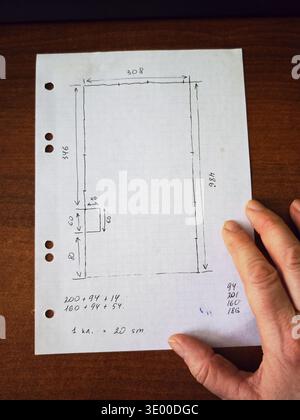 Kirov, Russia - February 11, 2026: A hand holds a layout drawing on white paper. The drawing includes measurements for the walls and a door. Numbers a Stock Photo