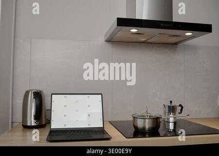 Laptop Placed on Countertop next to Cooking Pot and Coffee Maker in Kitchen  Stock Photo
