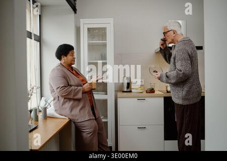 Senior Caucasian Man Talking with Middle Aged Black Woman in Modern Kitchen Stock Photo