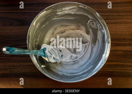 Top view of a metal mixing bowl with leftover whipped cream and a silicone spatula inside. Stock Photo